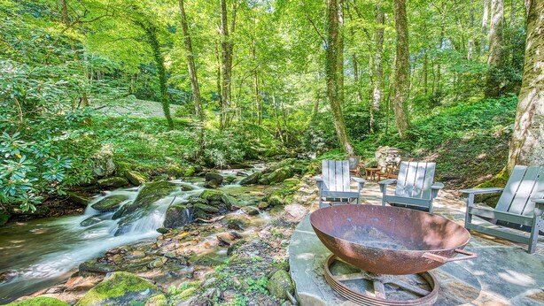 A forested area with a stream, outdoor seating, and a fire pit.