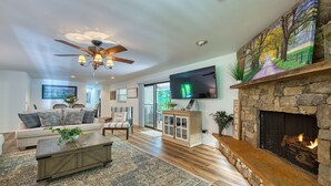 A spacious living room with a fireplace, a ceiling fan, and a television mounted on the wall.