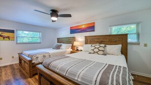 A bedroom with two beds, wooden headboards, a ceiling fan, and a painting of a sunset.