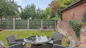 Une terrasse dotée de meubles en osier et d’une table en verre, entourée d’un mur de briques et d’une clôture en bois.