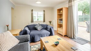 Ein Wohnzimmer mit einer Couch, einem Couchtisch, einem Bücherregal und einem Fenster mit Vorhängen.