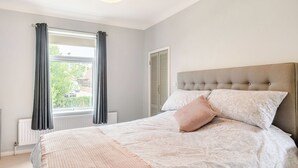 Ein Schlafzimmer mit einem großen Bett, einem Fenster mit Vorhängen, einem Heizkörper und einer Deckenleuchte.