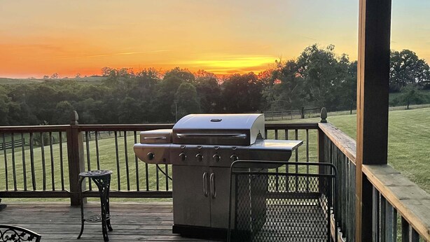 Una parrilla para barbacoa en una terraza de madera con vistas a un atardecer.