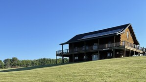 Una cabaña de dos pisos con balcón, paneles solares y una colina cubierta de hierba al frente.