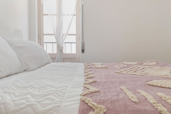 A bed with a white quilt and a pink blanket with a textured pattern.