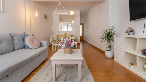 A living room with a sofa, a coffee table with a floral arrangement, a hanging chair, and a television on the wall. - Sweet 2-Bedroom Townhouse (Lagos)
