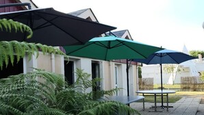 Een terras buiten met twee parasols, een tafel en varens.