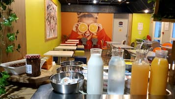 A juice bar with various beverages and condiments, a mural on the wall, and a seating area with tables and chairs.