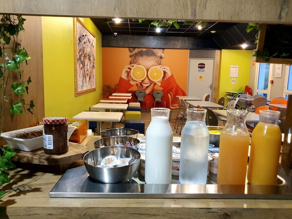 Un bar à jus proposant une variété de boissons et d’accompagnements, une fresque murale et un espace détente avec des tables et des chaises.