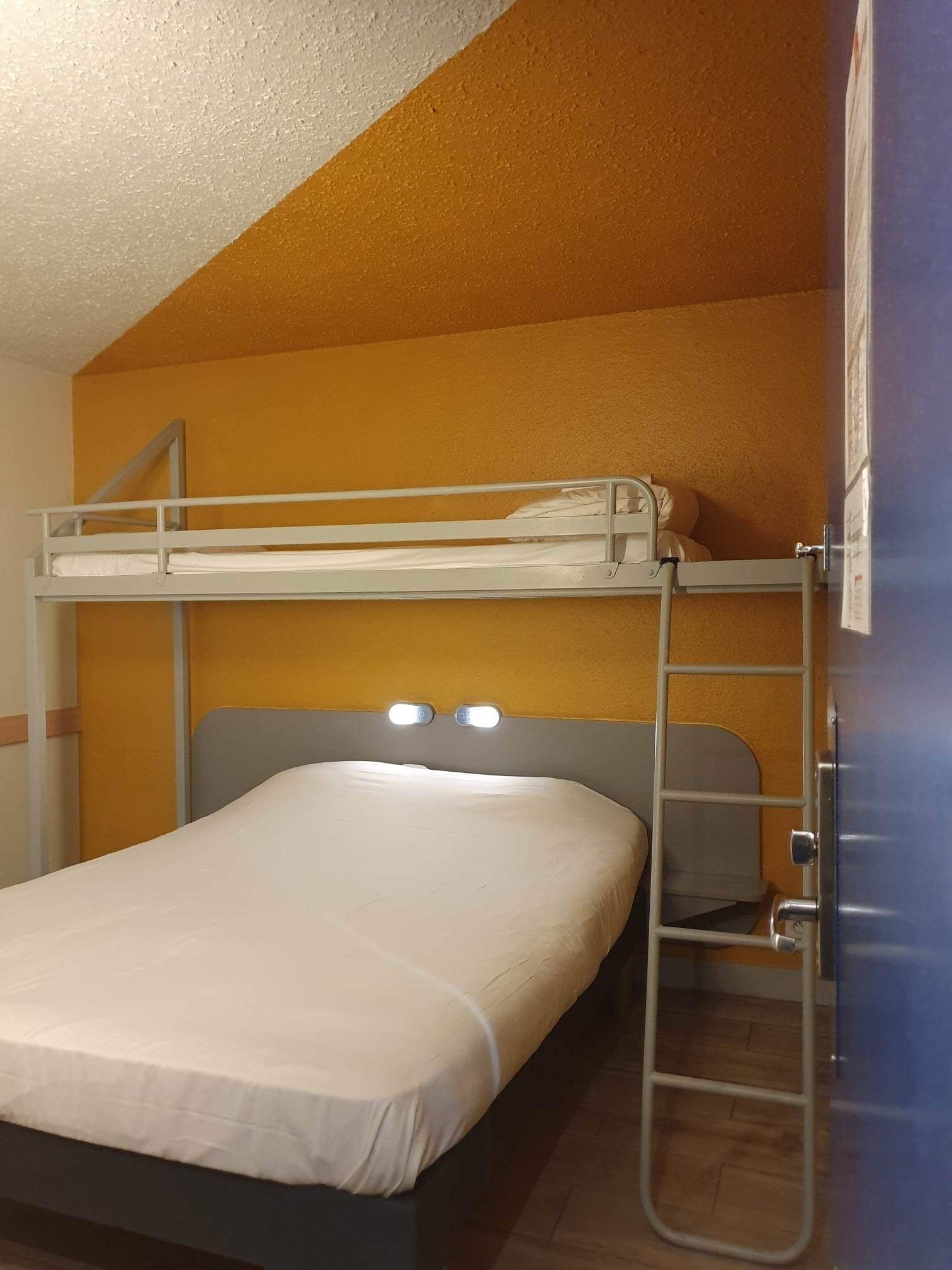 Een stapelbed met een ladder, een hoofdeinde met verlichting en een houten vloer.