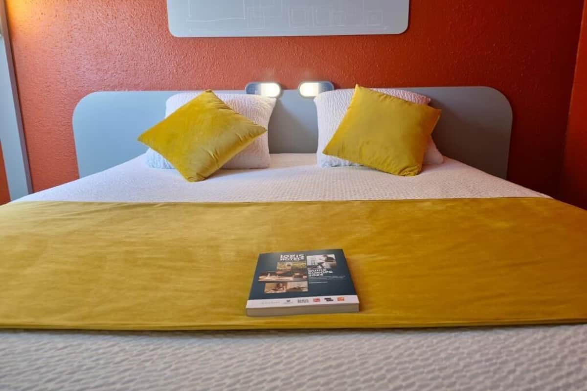 Un lit avec deux oreillers, une couverture jaune et un livre posé sur le lit.
