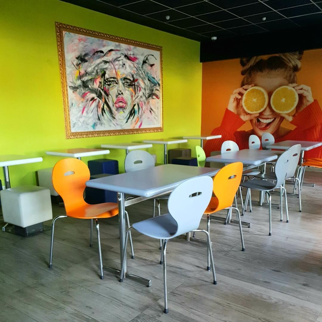 Un comedor moderno con mesas y sillas, un mural colorido en la pared y un techo con diseño de cuadrícula.