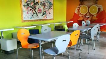 Un comedor moderno con mesas y sillas, un mural colorido en la pared y un techo con diseño de cuadrícula.
