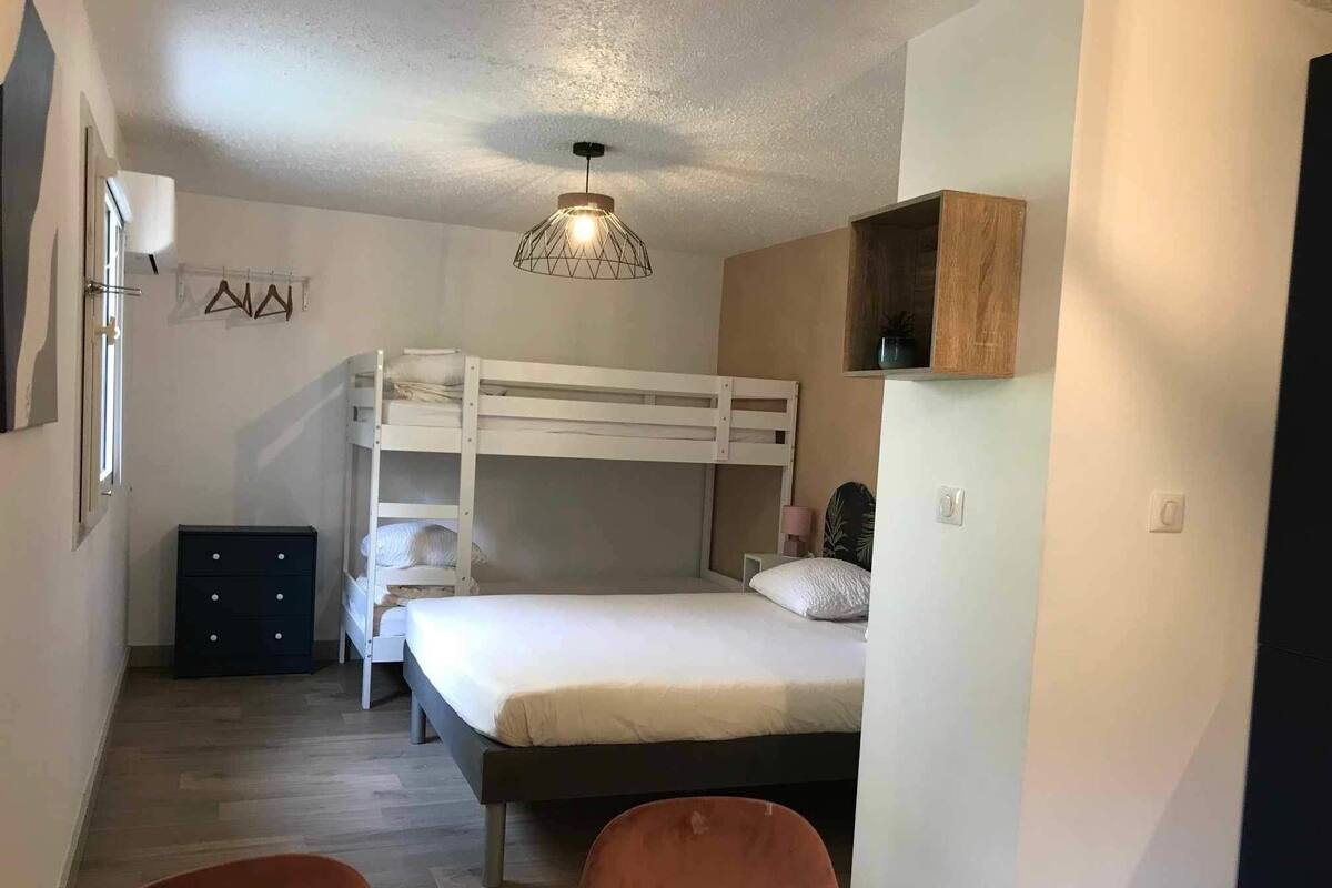 Une chambre de dortoir avec des lits superposés, un bureau et une chaise. On y trouve une commode, un luminaire suspendu et une étagère avec une plante.