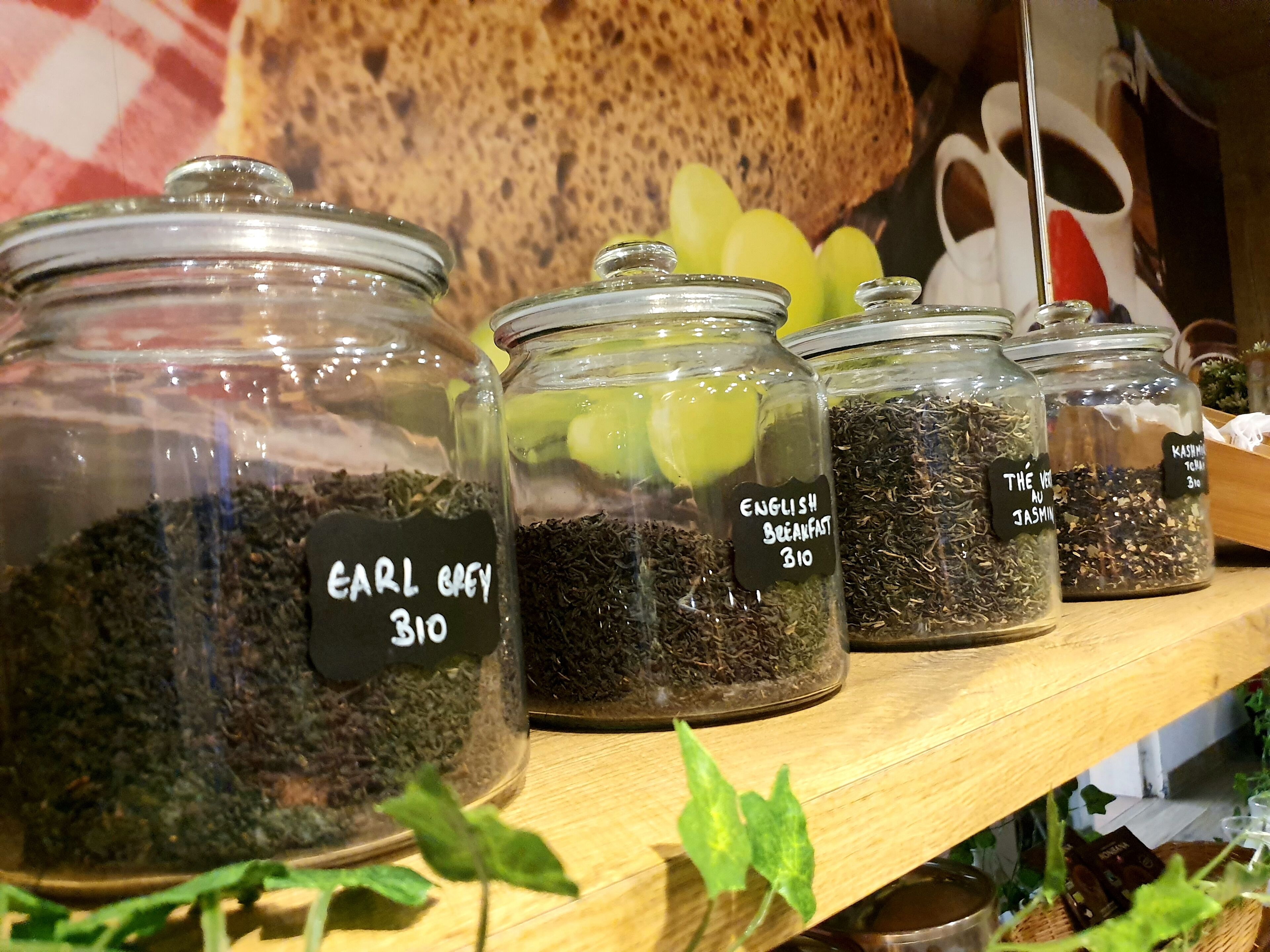 Glass jars labeled with different types of tea on a wooden shelf.