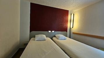 A hotel room with two single beds, a red accent wall, and a wall-mounted light fixture.