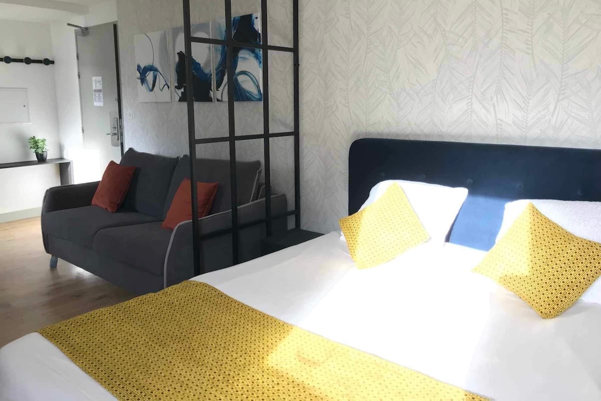 Une chambre d’hôtel comprenant un lit, un canapé, une cloison et un mur orné d’un motif de feuilles.