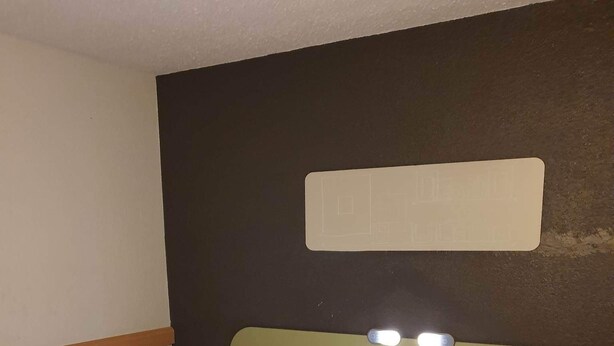 Een hotelkamer met een bed, een hoofdeinde met verlichting en een bedieningspaneel aan de muur.