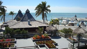 Un resort con un edificio de techo de paja, una terraza de madera con macetas y un puerto deportivo con barcos.