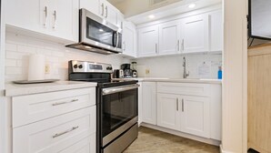 Una cocina compacta con armarios blancos, un microondas de acero inoxidable, una estufa y una cafetera.