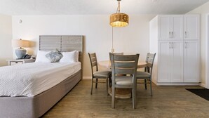 Un dormitorio con cama, mesita de noche, lámpara y un rincón comedor con mesa y sillas.