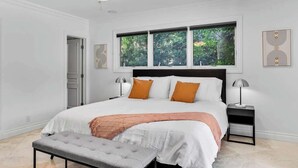 A bedroom with a large bed, two bedside tables, a bench, a ceiling fan, and a window with a view of trees. - Heated Pool 3BR Home · 4 Min to Hollywood Beach (Hollywood)