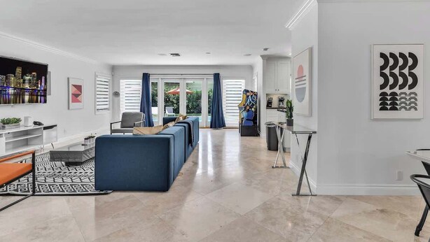 A spacious living area with a modern design, featuring a large sofa set, a dining table, and a kitchen area visible through a glass door. - Heated Pool 3BR Home · 4 Min to Hollywood Beach (Hollywood)