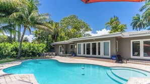 A swimming pool with a curved edge, surrounded by lounge chairs and a covered patio area. - Heated Pool 3BR Home · 4 Min to Hollywood Beach (Hollywood)
