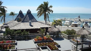 Een resort met een gebouw met rieten dak, een houten terras met plantenbakken en een jachthaven met boten.