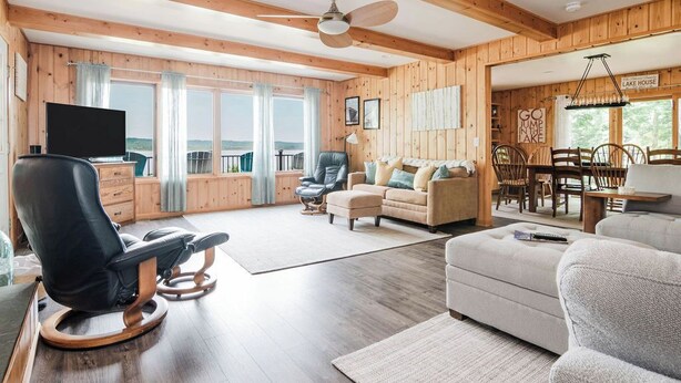 Ein geräumiges Wohnzimmer mit Holzbalkendecke, Deckenventilator, Flachbildfernseher, Sofa, Sessel und einer Essecke mit Holzkohlen und einem Tisch.