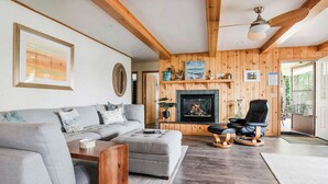 Ein Wohnzimmer mit grauem Sofa, einem Holztisch, einem Kamin und einem schwarzen Ledersessel.