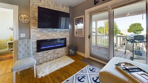 A modern living room with a stone fireplace, a flat-screen TV, a comfortable armchair, and a sign that reads "be our guest". - SSVR4-Downtown Munising Apartment, 2 blocks from Lake Superior (Munising)