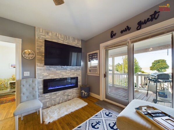 A modern living room with a stone fireplace, a flat-screen TV, a comfortable armchair, and a sign that reads "be our guest".
