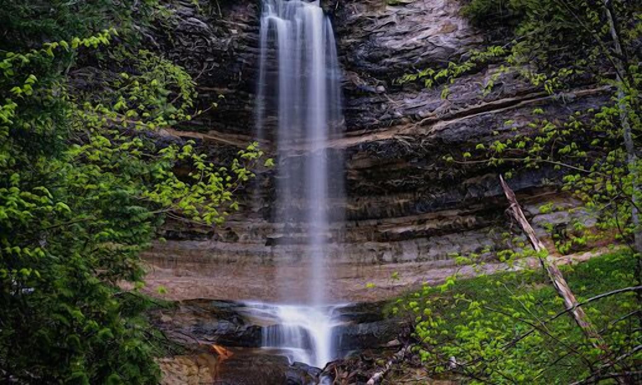 Une cascade se déversant le long d’une falaise rocheuse, entourée d’une végétation luxuriante.