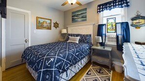 A bedroom with a bed, a desk, a chair, a ceiling fan, a window with curtains, and nautical-themed decor. - SSVR4-Downtown Munising Apartment, 2 blocks from Lake Superior (Munising)