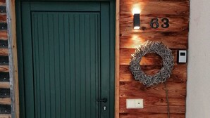 Uma porta verde com o número '63' acima, uma grinalda na parede e uma pequena luminária.
