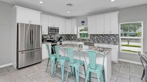 Una cocina moderna con armarios blancos, un refrigerador de acero inoxidable, un microondas y una isla grande con taburetes de bar.