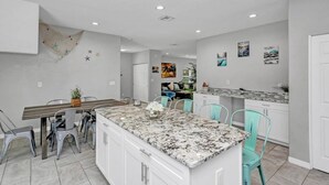 Una cocina moderna con armarios blancos, una isla de granito y sillas color turquesa.