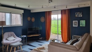 Un salon avec un canapé, un fauteuil, un téléviseur, une petite table et une fenêtre avec des rideaux.