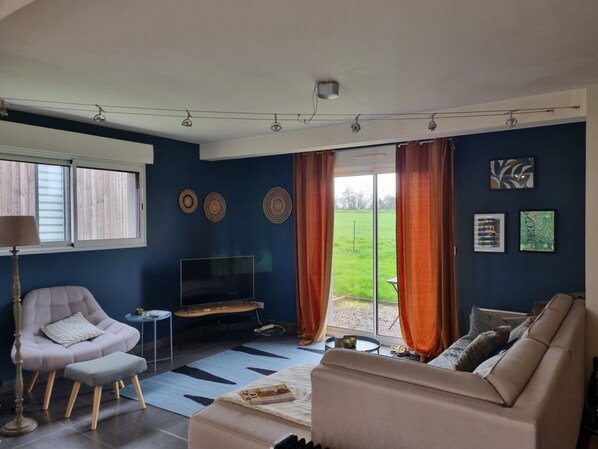 A living room with a sofa, a chair, a TV, a small table, and a window with curtains.