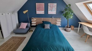 Une chambre avec un plafond en pente, un lit avec une literie de couleur turquoise, un bureau avec une chaise et deux œuvres d’art encadrées accrochées au mur.