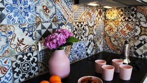 Une cuisine avec un plan de travail noir, un vase rose contenant des fleurs, des oranges et un bol de biscuits.