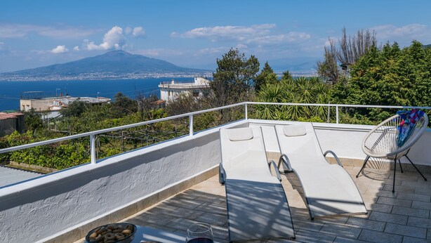 Une terrasse sur le toit offrant une vue sur la montagne et la mer, avec un fauteuil et un bol de collations.
