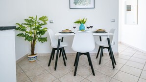 En matplats med ett vitt bord, fyra vita stolar, en krukväxt och ett inramat konstverk på väggen.