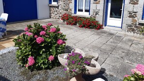 A stone building with a blue door and windows, surrounded by a garden with pink and red flowers. - Maison Bord de mer avec Jardin clos 3 CH/7 Personnes Plage à 550m (HILLION)