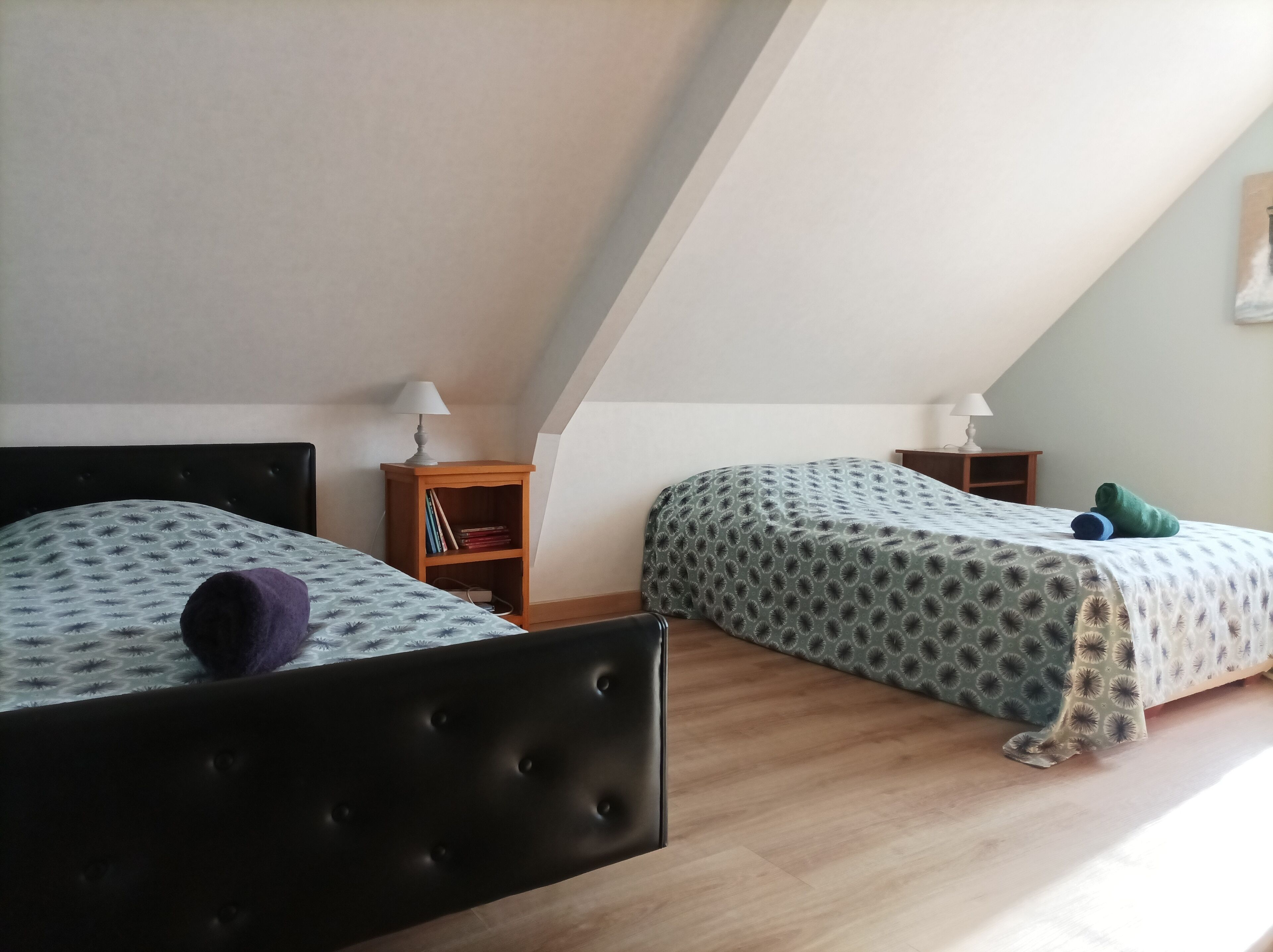 A room with two beds, a small wooden nightstand, and a lamp.