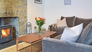 A cozy living room with a stone fireplace, a grey sofa, and a wooden coffee table. - 5 bedroom accommodation in New Quay (New Quay)