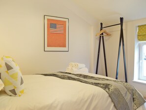 A neatly made bed with a patterned blanket, a framed American flag on the wall, and a window with a yellow curtain. - 5 bedroom accommodation in New Quay (New Quay)