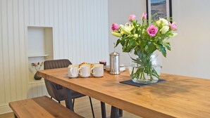 A wooden dining table with a vase of flowers, a coffee pot, and a framed picture on the wall. - 5 bedroom accommodation in New Quay (New Quay)