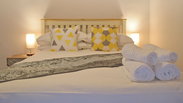 A neatly made bed with pillows, a blanket, and rolled towels. - 5 bedroom accommodation in New Quay (New Quay)